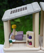 The PlanToys Planspace bedroom shown with two wooden peg dolls, a Grapat Nin and a Grimm's friend laying in the wooden bed.