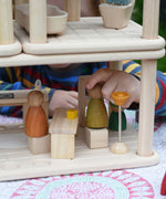 A close up of a child placing Grapat Nins wooden peg dolls on the seats from the PlanToys Planspace kitchen and dining room set. 