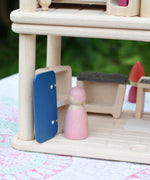 A close up of a Grimm's friends wooden peg dolls standing in front of a PlanToys PlanSpace wooden toy fridge that appears empty.