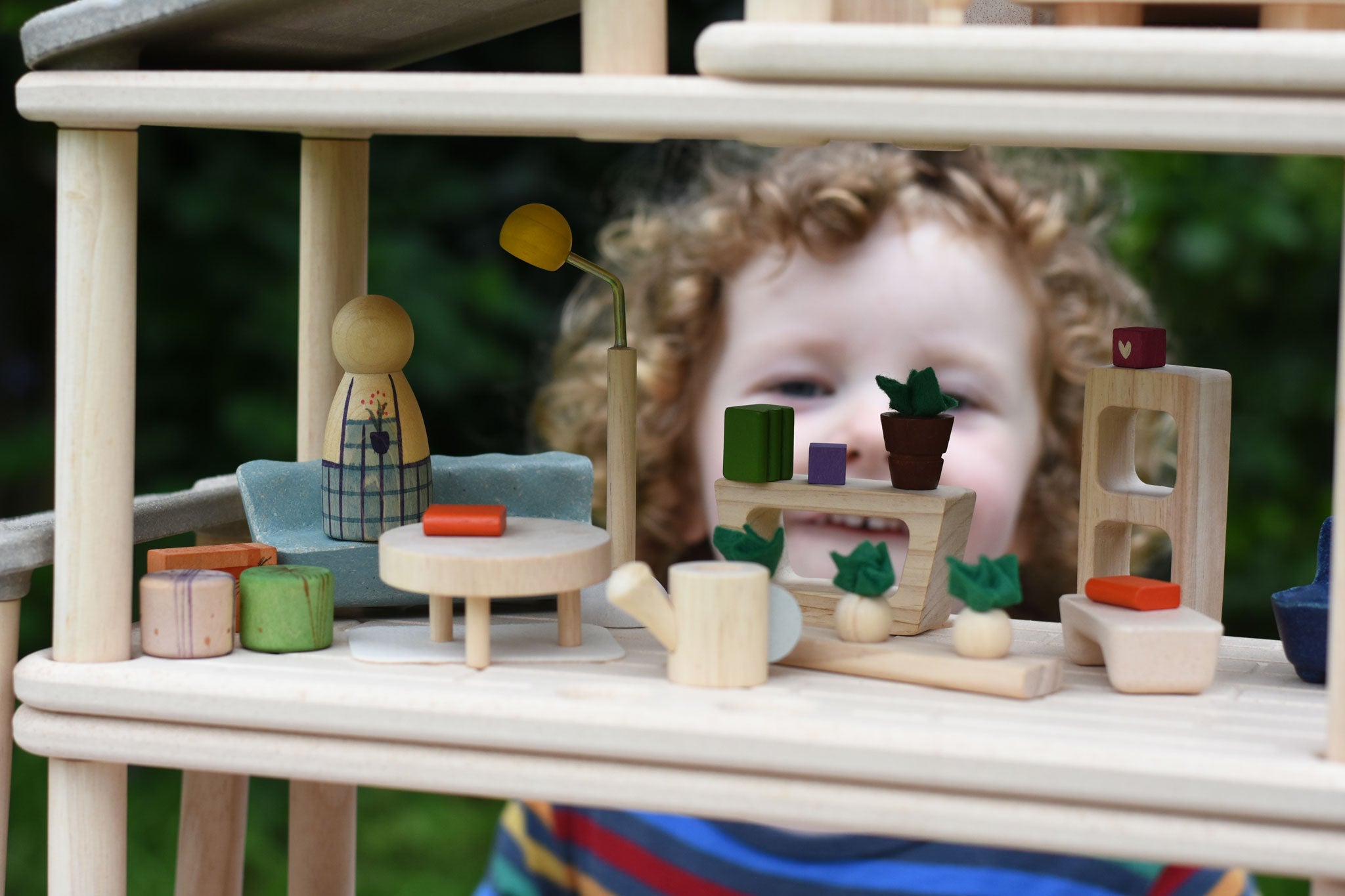 The Plan Toys PlanSpace living room set, stacked on other sets from the modular PlanSpace range. A wooden peg doll has been placed on the sofa. A child can be seen looking on the background.