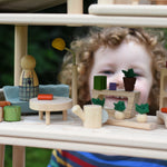 The Plan Toys PlanSpace living room set, stacked on other sets from the modular PlanSpace range. A wooden peg doll has been placed on the sofa. A child can be seen looking on the background.