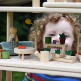 The Plan Toys PlanSpace living room set, stacked on other sets from the modular PlanSpace range. A wooden peg doll has been placed on the sofa. A child can be seen looking on the background.