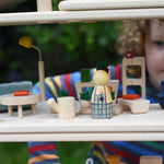 The Plan Toys PlanSpace living room set, stacked on other sets from the modular PlanSpace range. A wooden peg doll has been placed at the front. A child can be seen in the background.