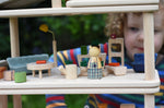 The Plan Toys PlanSpace living room set, stacked on other sets from the modular PlanSpace range. A wooden peg doll has been placed at the front. A child can be seen in the background.