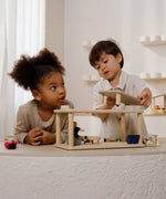 2 children playing the with Plantoys wooden planspace living room set on a concrete surface showing the sunlight piece being out on top of the living room