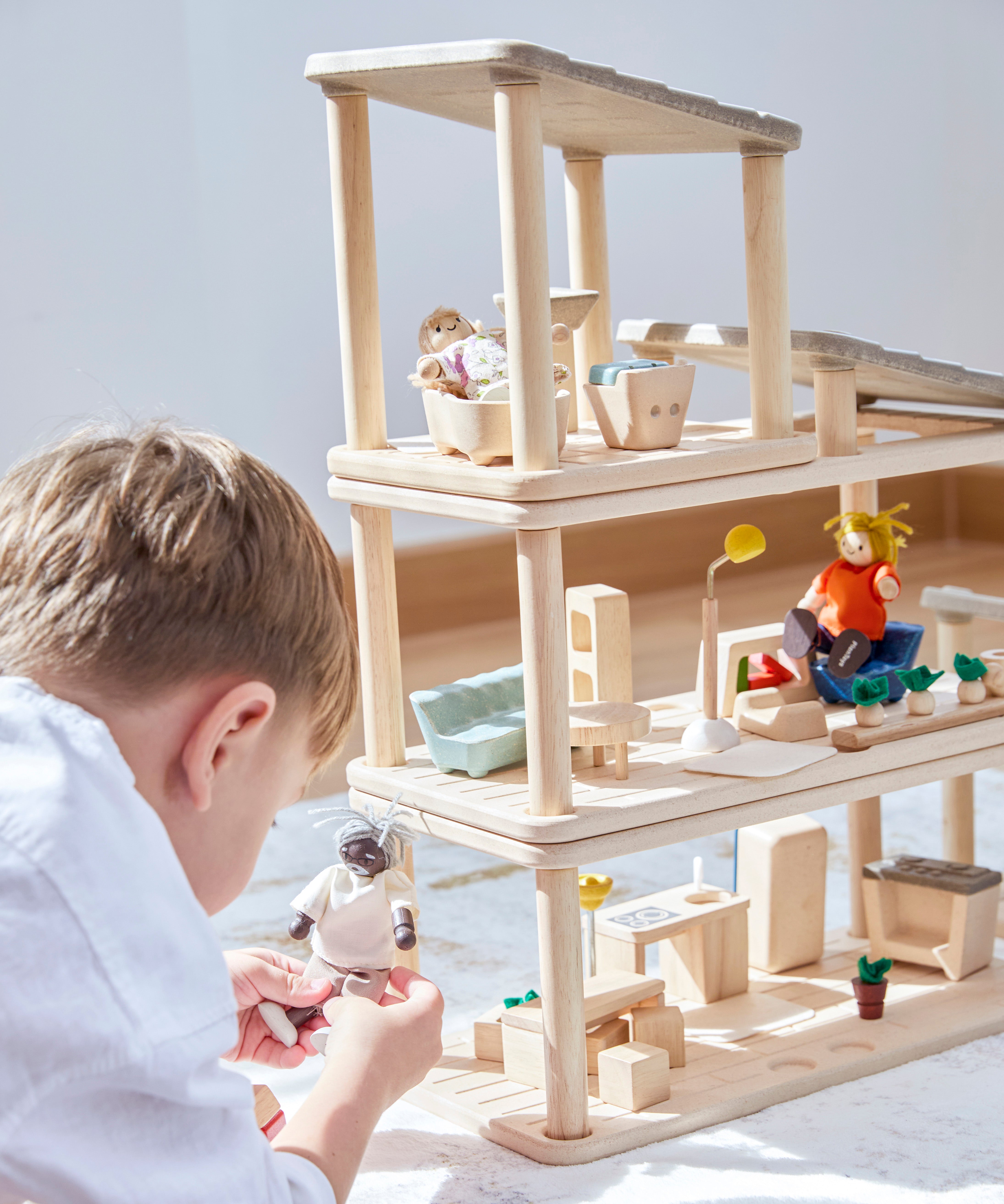 A close up of a child playing the with Plantoys wooden planspace  set that stacked  on top of eachother to create a dollhouse, showing all of the accessories and some of the PlanToys family dolls 