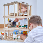 2 children playing playing the with Plantoys wooden planspace set that's stacked on top of eachother to create a dollhouse, showing all of the accessories and some of the PlanToys family dolls 
