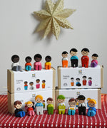A collection of different PlanToys PlanWorld wooden doll family sets. The dolls are shown on and besides the boxes.