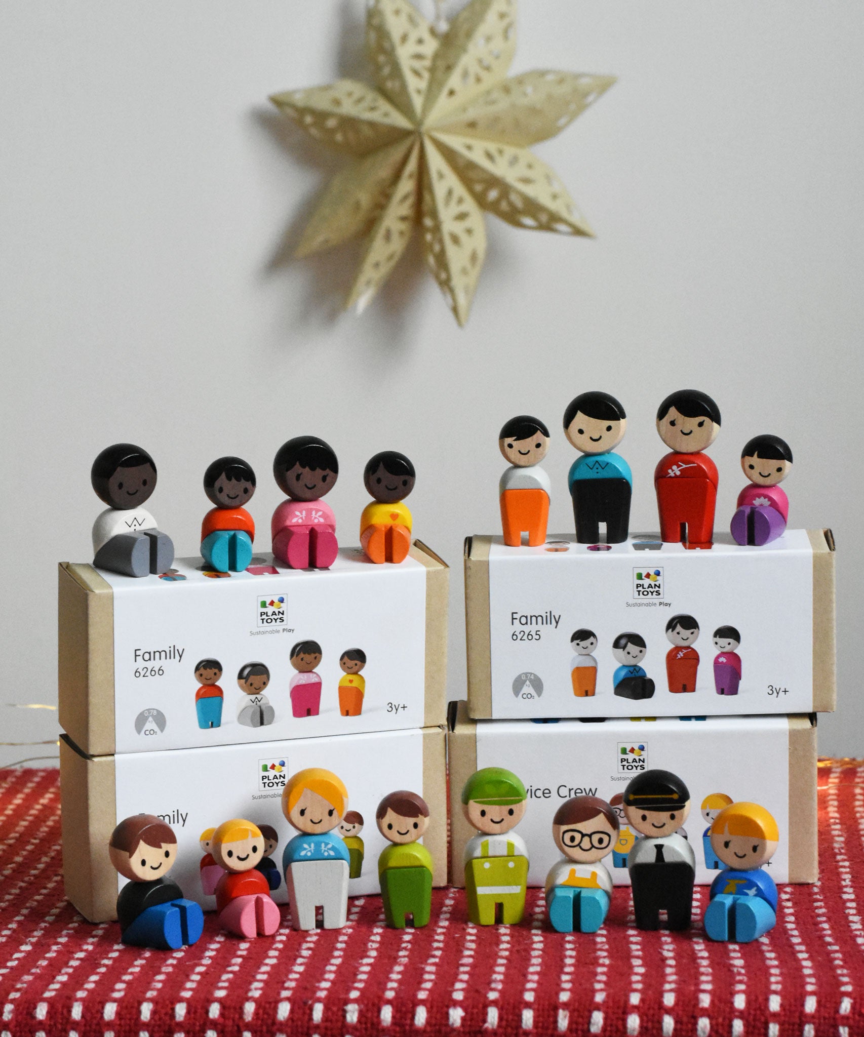 A collection of different PlanToys PlanWorld wooden doll family sets. The dolls are shown on and besides the boxes.
