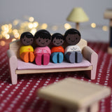The PlanToys PlanWorld wooden doll family with black Skin and black Hair in a seated position placed on a PlanToys wooden sofa. 