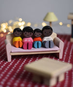 The PlanToys PlanWorld wooden doll family with black Skin and black Hair in a seated position placed on a PlanToys wooden sofa. 