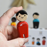 The woman from PlanToys PlanWorld wooden doll family with White Skin and black Hair in an adult's hand. 