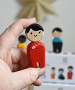The woman from PlanToys PlanWorld wooden doll family with White Skin and black Hair in an adult's hand. 