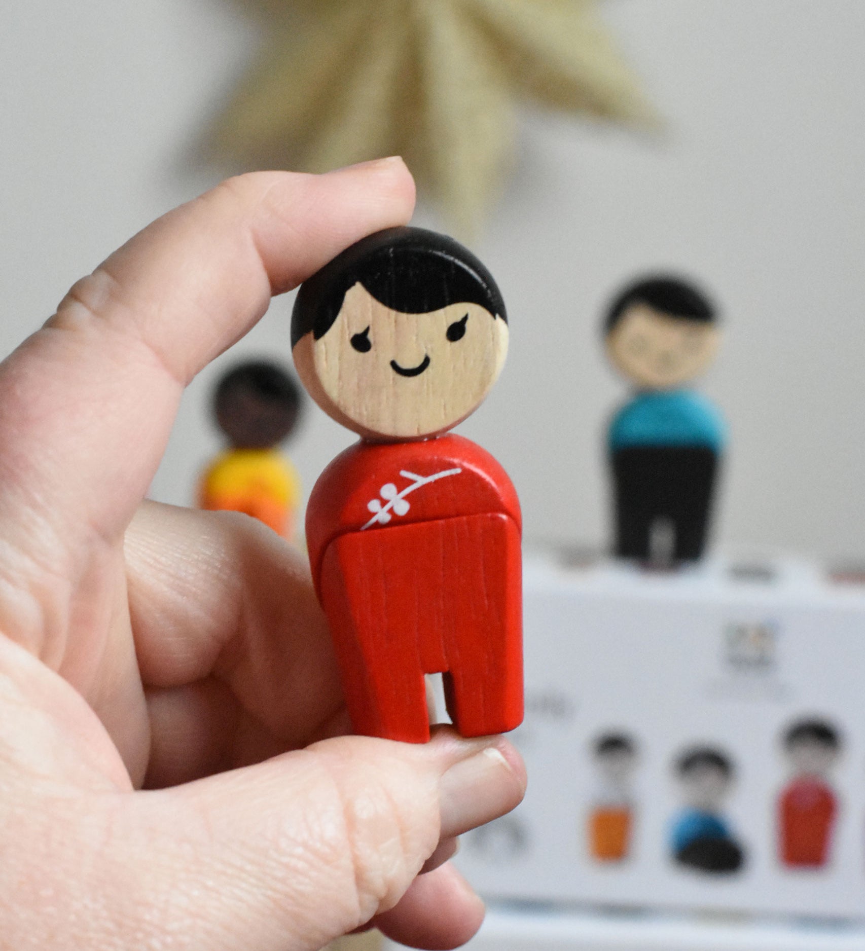 The woman from PlanToys PlanWorld wooden doll family with White Skin and black Hair in an adult's hand. 