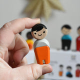 The boy from PlanToys PlanWorld wooden doll family with White Skin and black Hair in an adult's hand. 