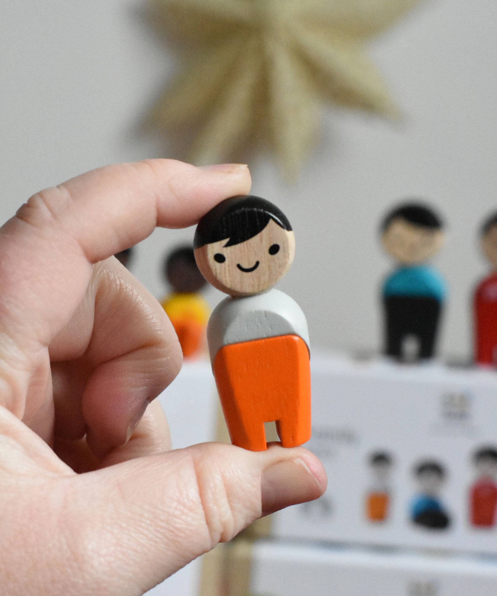The boy from PlanToys PlanWorld wooden doll family with White Skin and black Hair in an adult's hand. 