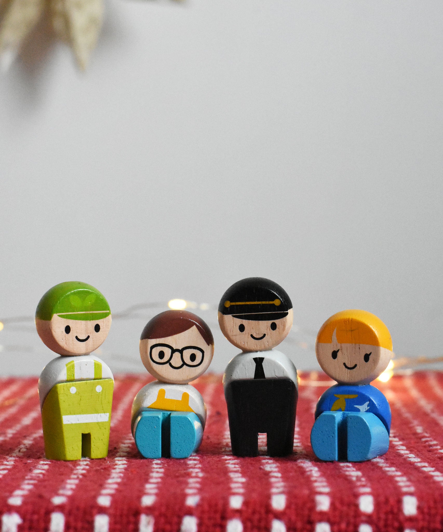 The PlanToys PlanWorld wooden doll service crew on a red surface, two are in a standing position and two are seated.