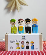 The PlanToys PlanWorld wooden doll service crew in a standing position placed on the cardboard packaging box. 