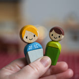 An adult and a child doll from the PlanToys PlanWorld wooden doll family set with White Skin, Brown and Blonde Hair shown in an adult's hand. 