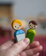 An adult and a child doll from the PlanToys PlanWorld wooden doll family set with White Skin, Brown and Blonde Hair shown in an adult's hand. 