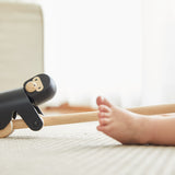 Close up of the PlanToys wooden gorilla pull along toy on a white carpet next to a child's feet