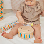 Close up of young child playing with the PlanToys solid wooden drum toy on a white blanket