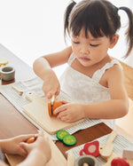 Young girl cutting pieces of play food with the wooden knife from the PlanToys charcuterie board set