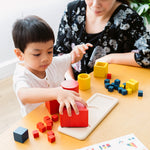 Child and woman sat at a table playing with the PlanToys wooden nesting and matching shapes set