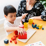 Child and woman sat at a table playing with the PlanToys wooden nesting and matching shapes set