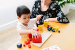 Child and woman sat at a table playing with the PlanToys wooden nesting and matching shapes set