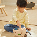 Young child sat on a wooden floor playing with the PlanToys miracle pounding toy