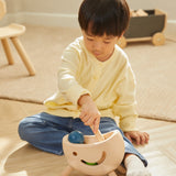 Young child sat on a wooden floor playing with the PlanToys miracle pounding toy