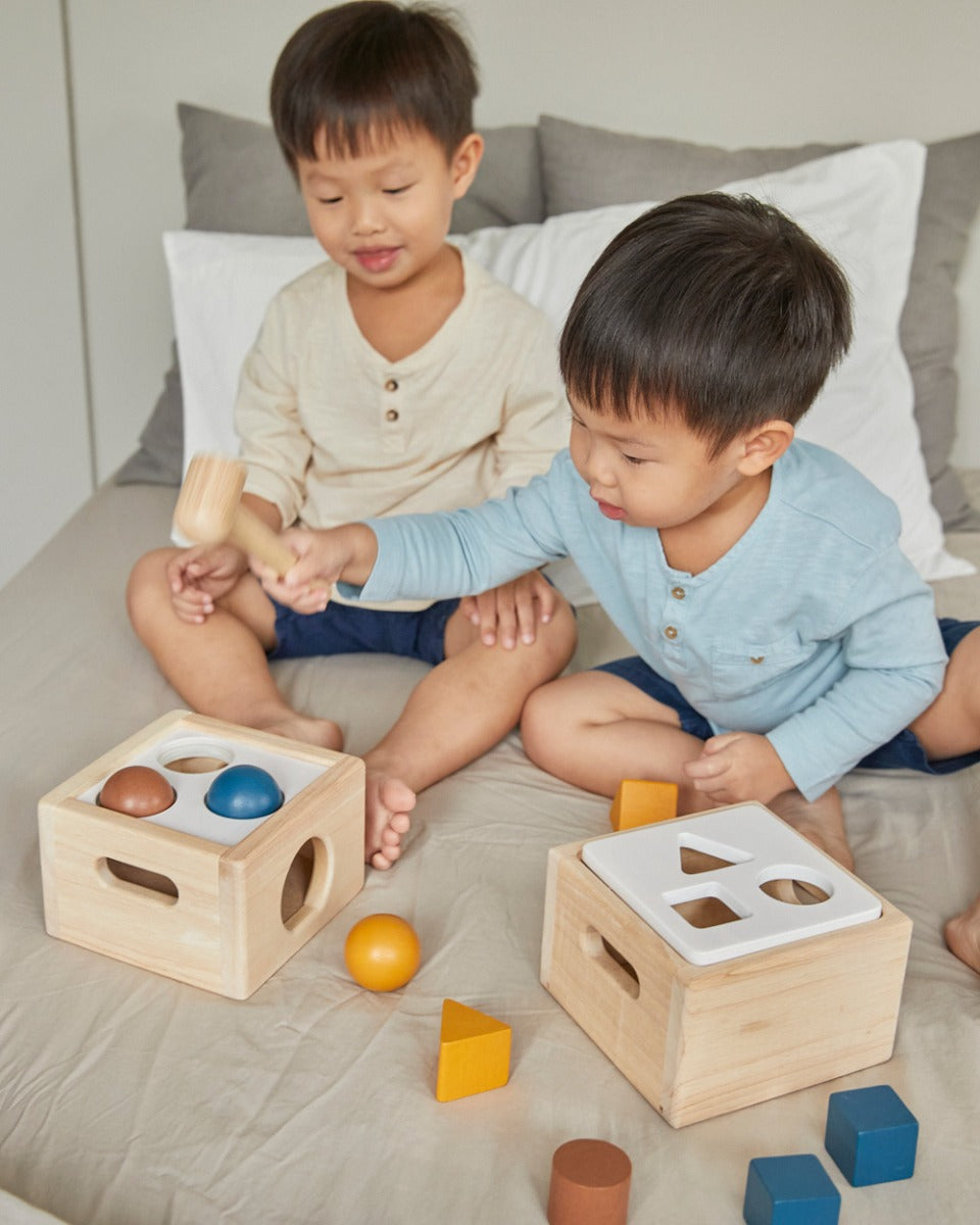 Two boys sat on a bed playing with the PlanToys wooden shape sorter toys