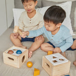 Two boys sat on a bed playing with the PlanToys wooden shape sorter toys