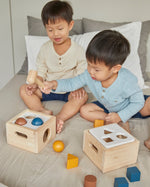 Two boys sat on a bed playing with the PlanToys wooden shape sorter toys