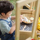Child sitting by a PlanToys play kitchen and playing with wooden eggs