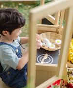 Child sitting by a PlanToys play kitchen and playing with wooden eggs