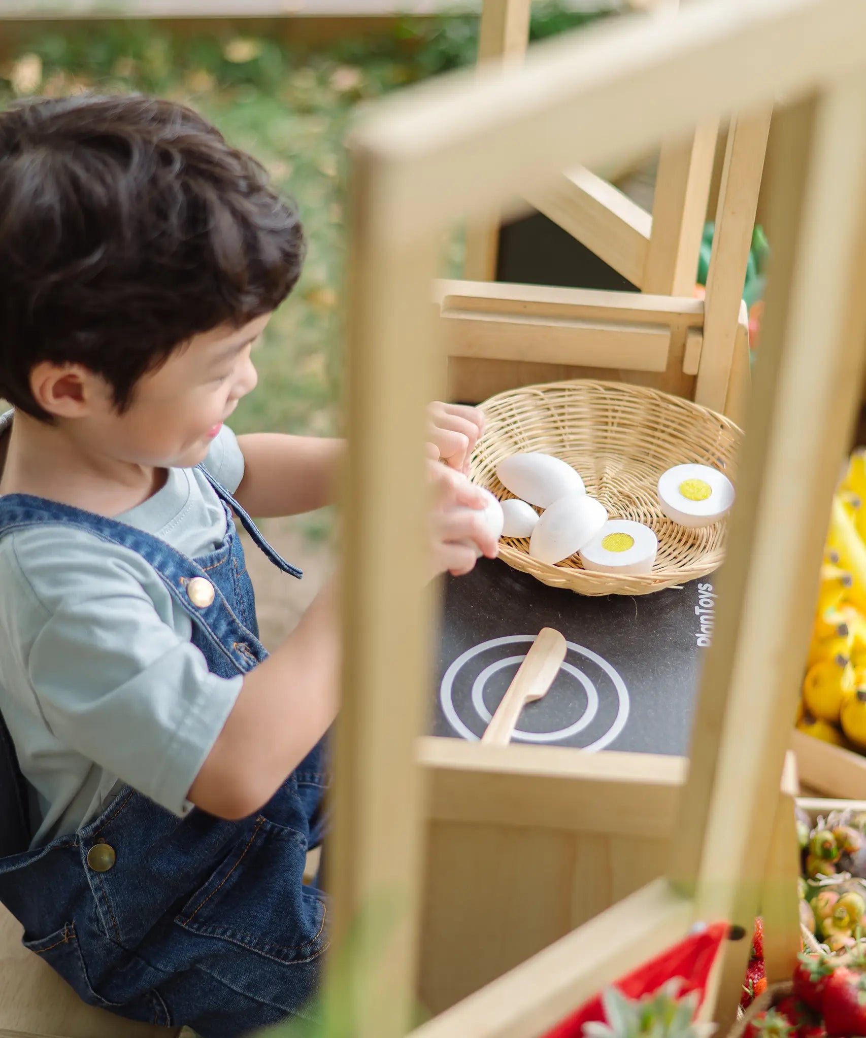 Child sitting by a PlanToys play kitchen and playing with wooden eggs