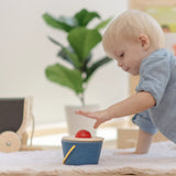 Baby playing with the PlanToys pop and drop wooden bucket baby posting toy pushing the red ball into the slot.