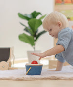 Baby playing with the PlanToys pop and drop wooden bucket baby posting toy pushing the red ball into the slot.