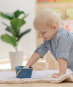 Baby playing with the PlanToys pop and drop wooden bucket baby posting toy putting their hand inside the bucket.