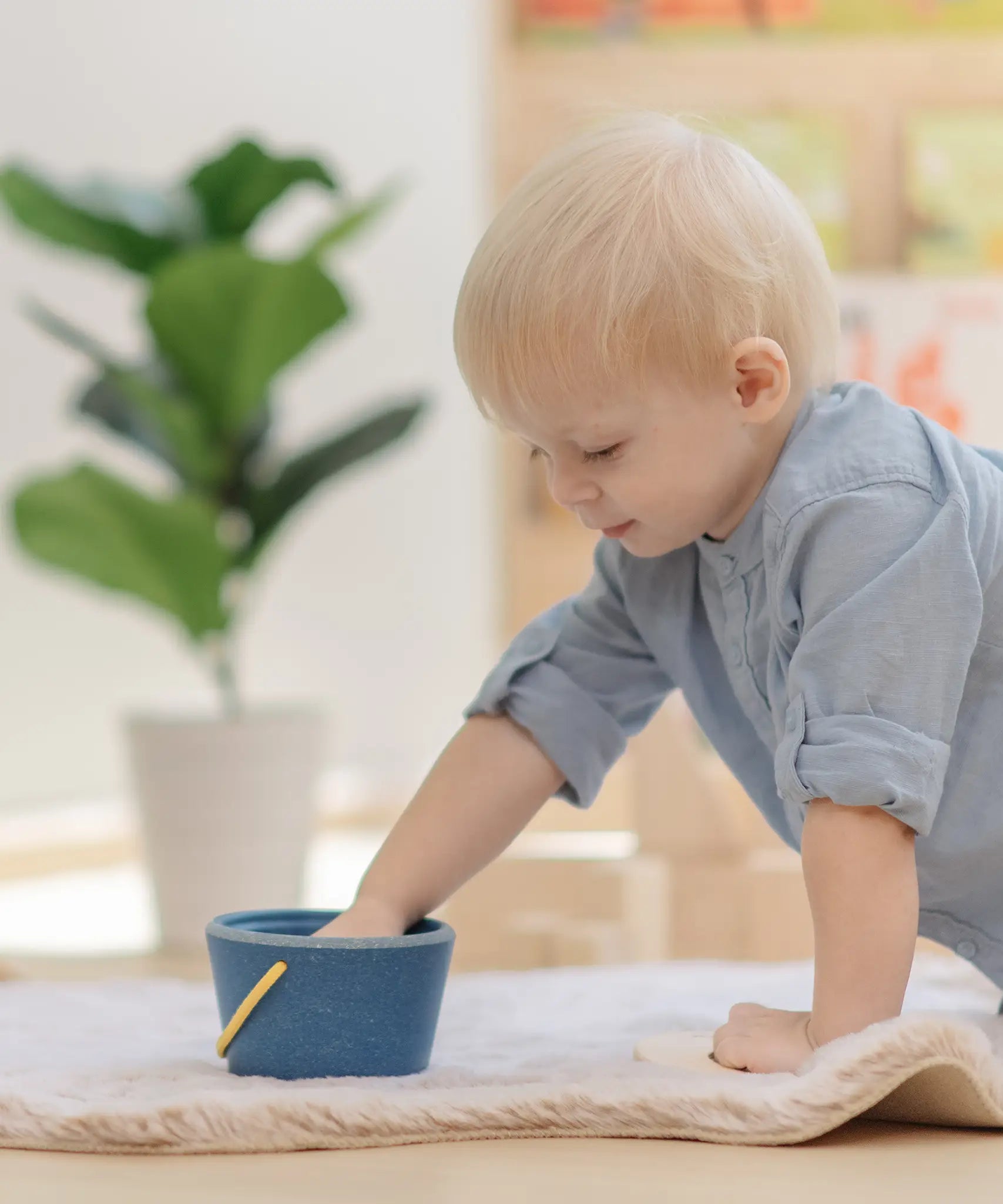 Baby playing with the PlanToys pop and drop wooden bucket baby posting toy putting their hand inside the bucket.