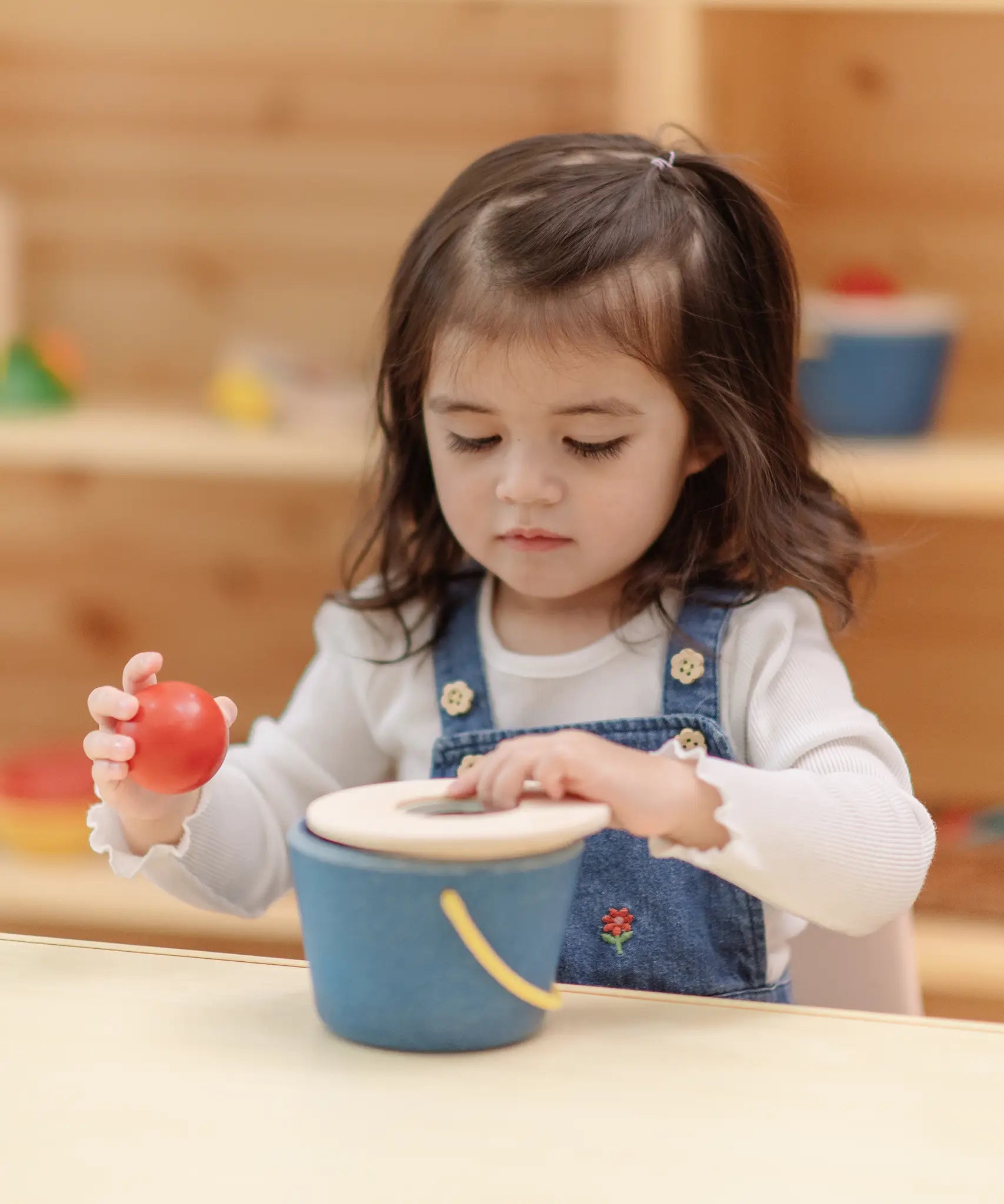Toddler playing with the PlanToys pop and drop wooden bucket baby posting toy.