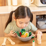 Child looking down at a PlanToys chef's salad bowl filled with play food at the table