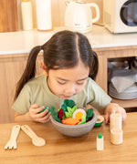 Child looking down at a PlanToys chef's salad bowl filled with play food at the table
