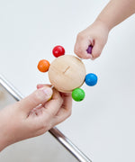 Two hands pulling at the beads of the Plan Toys Pull & Grasp wooden baby toy.