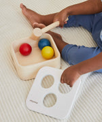 Overhead view of a child playing with the PlanToys punch and drop bin wooden pounding toy, taking the lid off the bin.