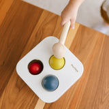 PlanToys punch and drop bin wooden pounding toy. Overhead view of a child pounding the yellow ball into the box.