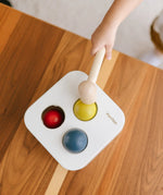 PlanToys punch and drop bin wooden pounding toy. Overhead view of a child pounding the yellow ball into the box.