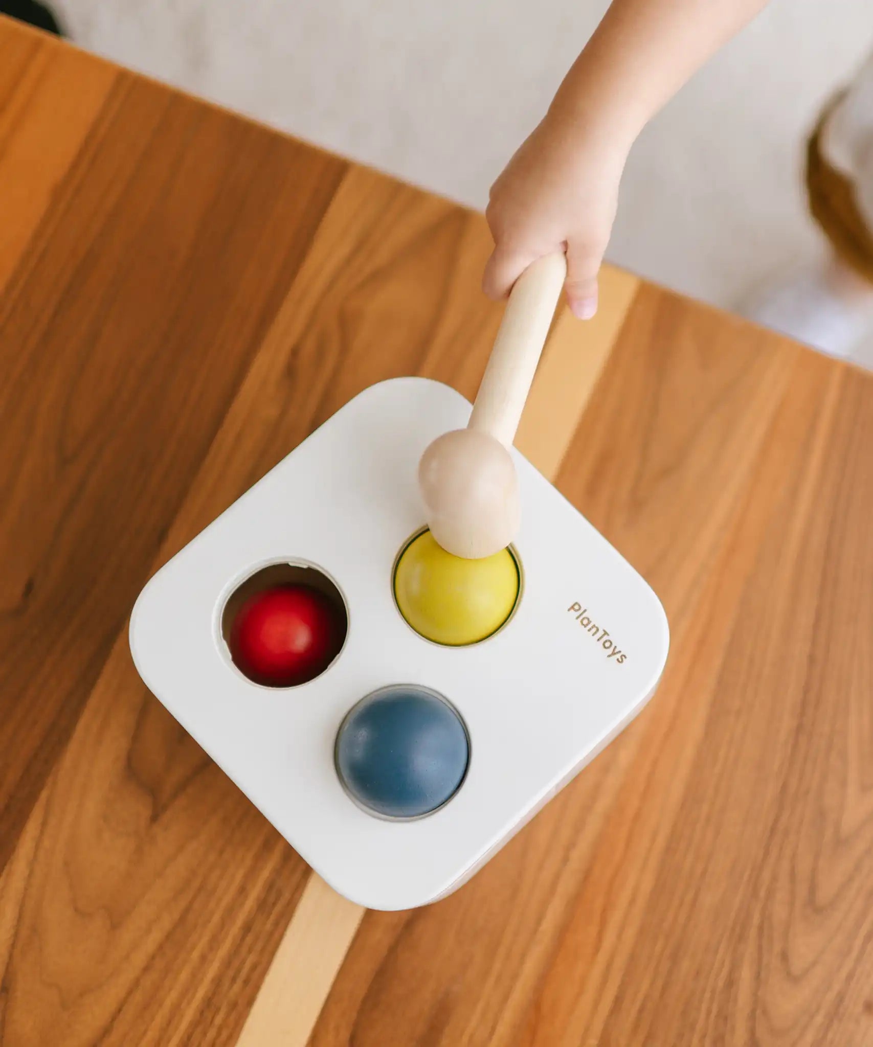 PlanToys punch and drop bin wooden pounding toy. Overhead view of a child pounding the yellow ball into the box.